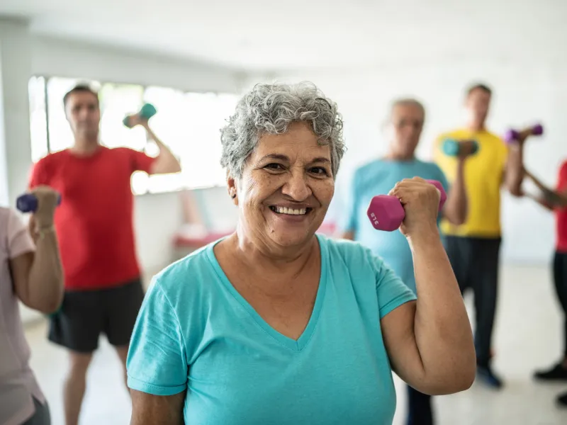 Senior woman smiling and lifting a free weight while in a group exercise class.